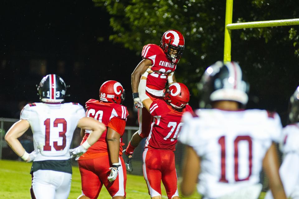 Manual High School running back Zah’Ron Washburn, middle, celebrates a touchdown with teammates Trey Ryan and Avery Williams during a football game Friday, Sept. 23, 2022, in Louisville, Ky. The Crimsons defeated Ballard 21-0.