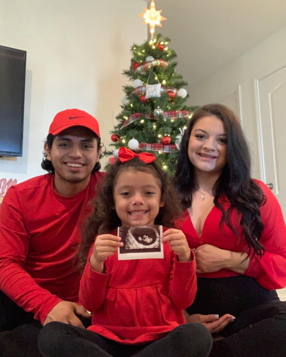 Jasmine and her partner posing for a photo with their daughter who's holding up the ultrasound of the baby