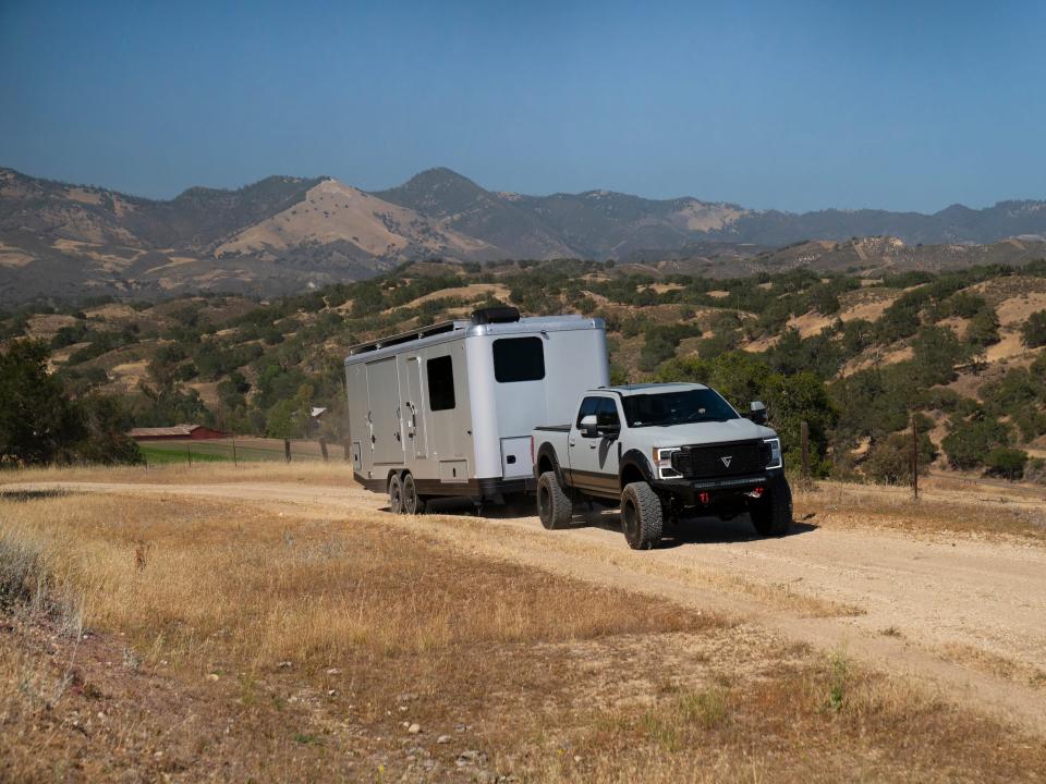 The travel trailer being towed by a truck on a dirt road near a field.