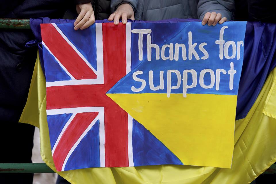 Royal fans hold a banner in the colors of the British and Ukrainian national flags and the inscription "Thanks for support" and wait in the rain at the Rathausmarkt in front of Hamburg City Hall for the arrival arrival of the British royals, Friday, March 31, 2023 . At the end of their three-day trip to Germany, Britain's King Charles III and Camilla Queen Consort visit the Hanseatic city of Hamburg. (Marcus Brandt/dpa via AP)