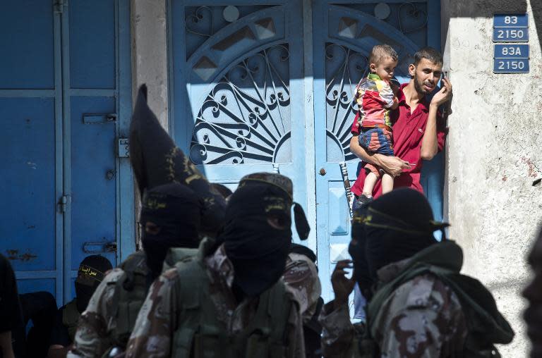 A Palestinian man holds a child in his arms as he watches Islamic Jihad militants parade in a street of Gaza City on August 29, 2014