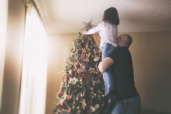 man lifting his daughter to the top of the christmas tree to place a star there