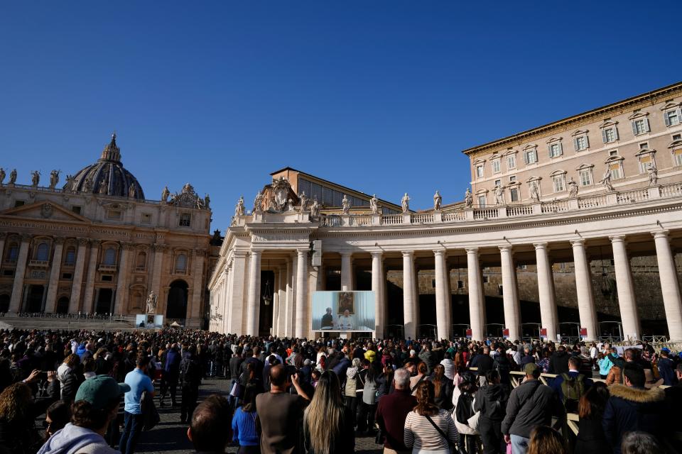 People watch Pope Francis on a giant monitor set up in St. Peter's Square at the Vatican on Dec. 3, 2023, as he blesses the faithful gathered in the square for the traditional Angelus noon prayer