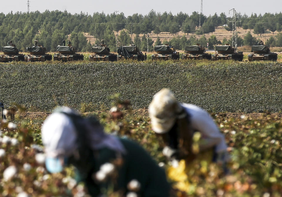Farmers gather cotton as Turkish army tanks are seen at a staging area close to the border with Syria in Sanliurfa province, southeastern Turkey, Thursday, Oct. 17, 2019. U.S. Vice President Mike Pence and State Secretary Mike Pompeo were scheduled to arrive in Ankara and press Turkey's President Recep Tayyip Erdogan to accept a ceasefire in northeast Syria. (AP Photo/Emrah Gurel)