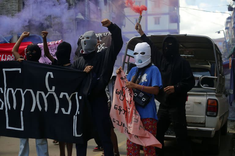 Jóvenes manifestantes gritan consignas y sostienen bengalas durante una protesta antigolpista en Yangon, Myanmar, el 25 de julio de 2022