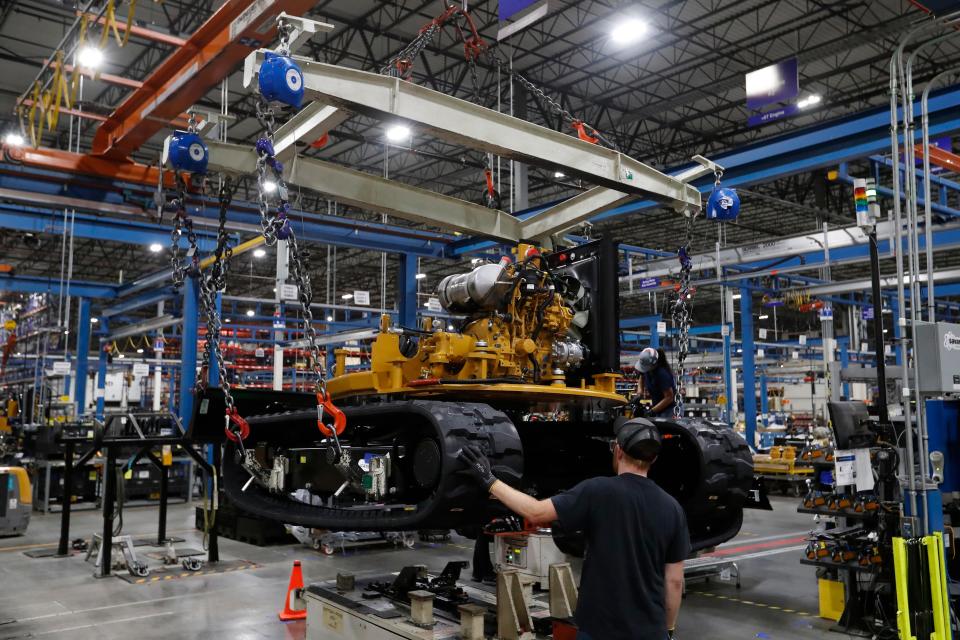 A worker moves an excavator's track system onto a robot that will move it into the next section of the assembly line at the Caterpillar plant.