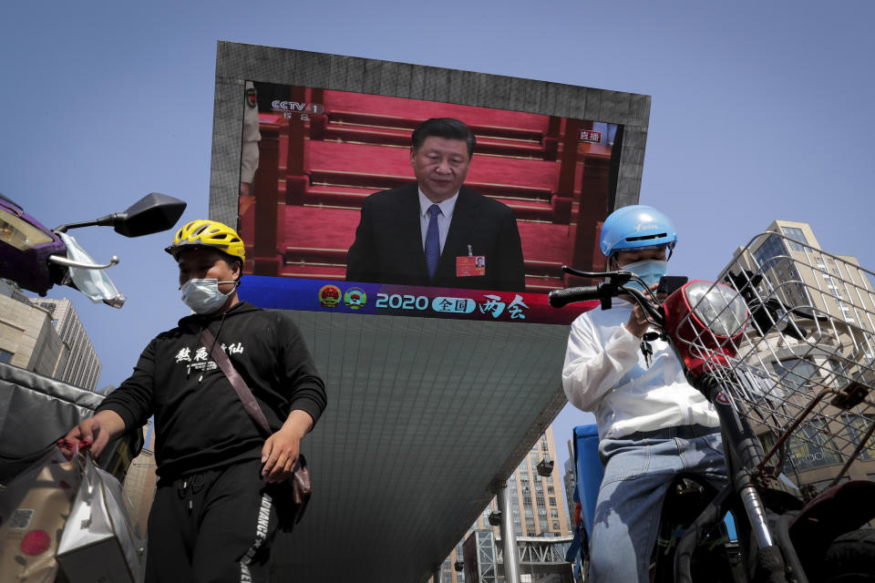 Dos repartidores de alimentos equipados con mascarillas para protegerse de la propagación del nuevo coronavirus cerca de un televisor gigante que muestra al presidente chino Xi Jinping en la ceremonia de clausura de la Asamblea Popular Nacional de China, en Beijing, el jueves 28 de mayo de 2020. (Foto AP/Andy Wong)