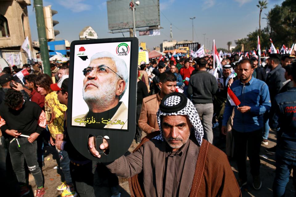 A supporter of Abu Mahdi al-Muhandis, deputy commander of the Popular Mobilization Forces, holds a photo of him during a protest in Tahrir Square, Iraq, Sunday, Jan. 3, 2021. Thousands of Iraqis converged on a landmark central square in Baghdad on Sunday to commemorate the anniversary of the killing of General Qassem Soleimani, head of Iran's Quds force and al-Muhandis in a U.S. drone strike. (AP Photo/Khalid Mohammed)