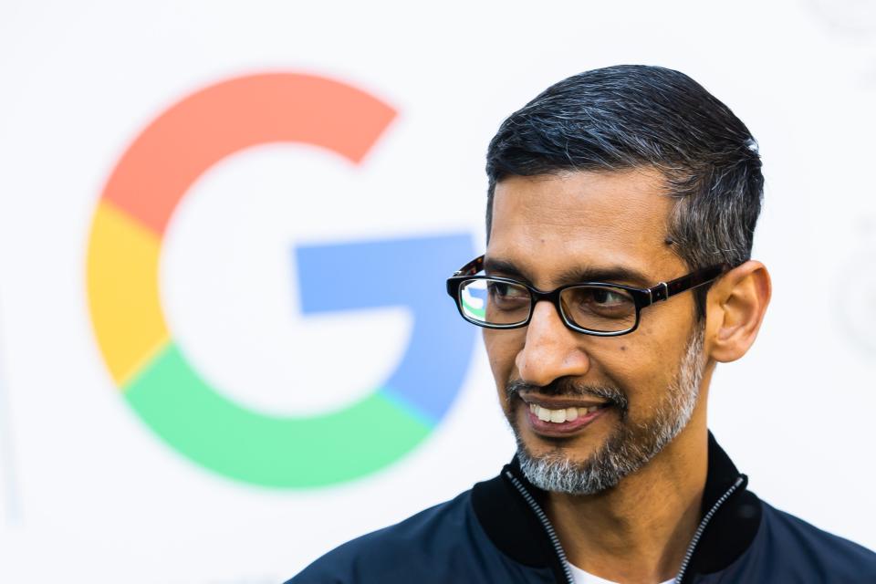 Google CEO Sundar Pichai stands in front of the Google logo.