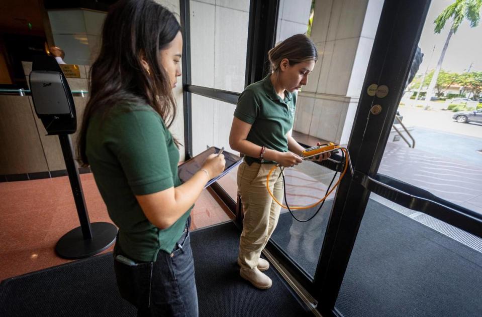 Los miembros del equipo de auditores de Industrial Assessment Center (IAC) de la Universidad de Miami (UM) Sophia Acon (a la izquierda) y Jessica Méndez (a la derecha) usando un caudalímetro para medir el flujo de aire que entra en el edificio por los huecos de las puertas principales.