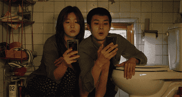 Two people squatting in a bathroom and scrolling on their phones