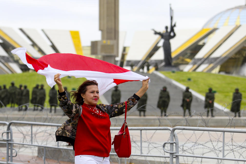 A woman waves an old Belarusian national flag as she a police line in front of a WWII memorial, during an opposition rally to protest the official presidential election results in Minsk, Belarus, Sunday, Sept. 27, 2020.Hundreds of thousands of Belarusians have been protesting daily since the Aug. 9 presidential election. (AP Photo/TUT.by)