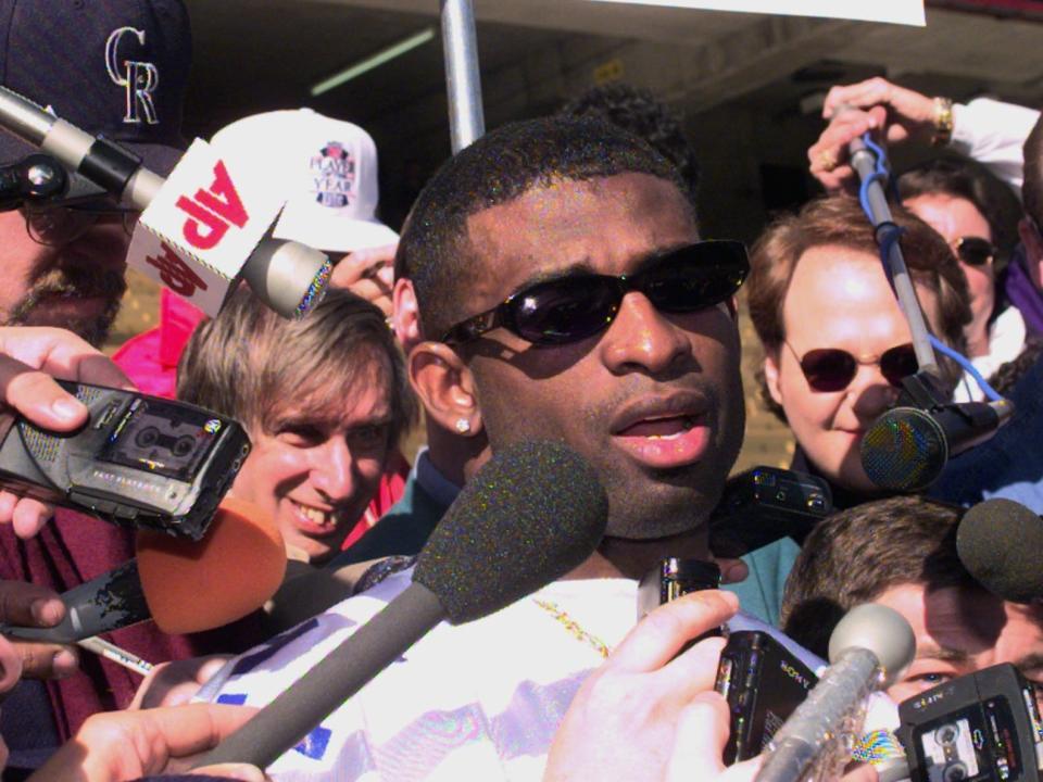 Deion Sanders is surrounded by members of the press.