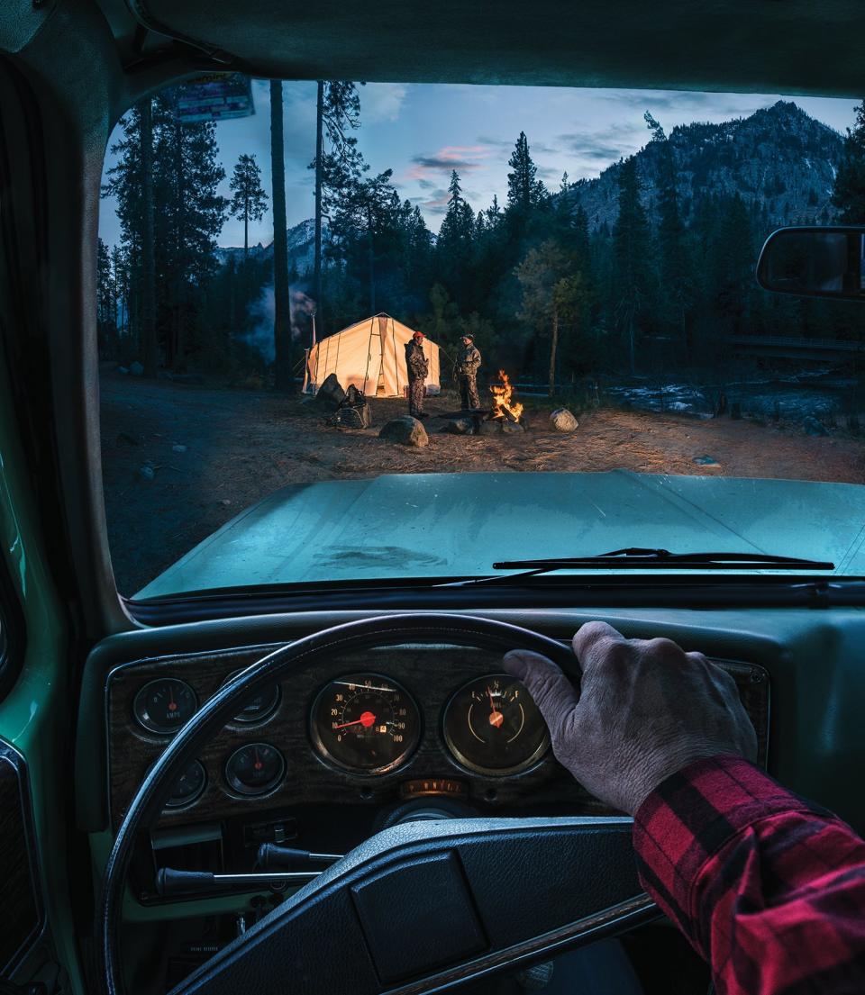 view through truck windshield of lit-up wall tent with several people outside