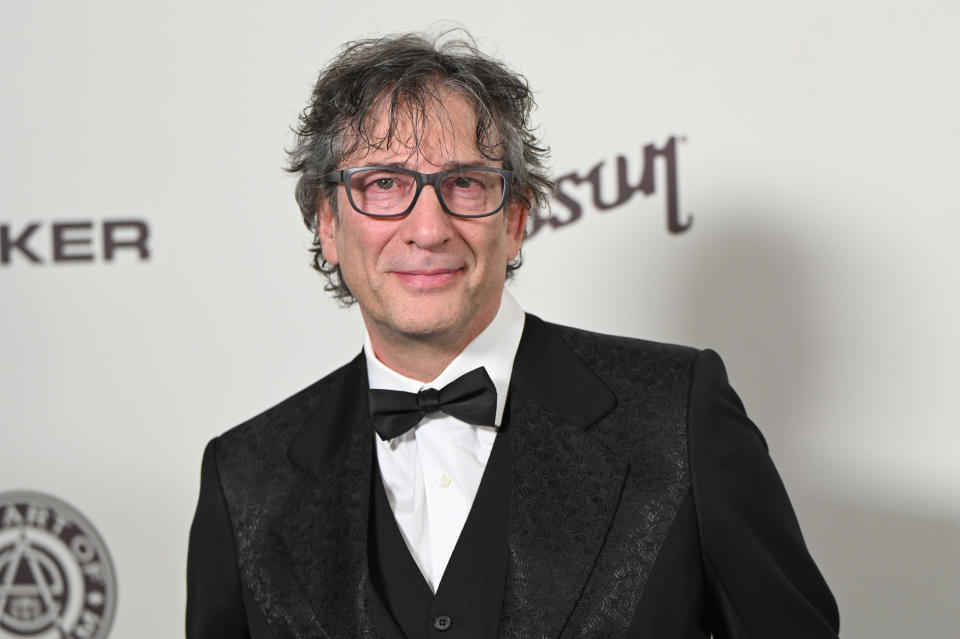 Neil Gaiman, wearing a black suit with a bowtie, poses at the red carpet event