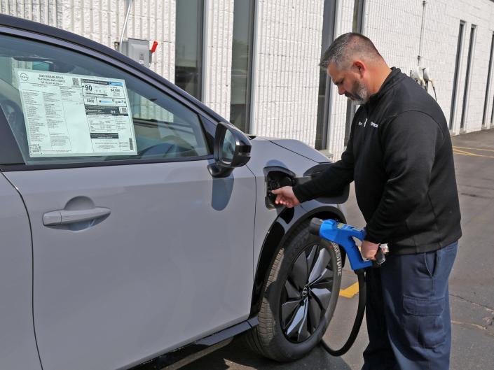 A dealership service director plugs an EV charger into an electric car.