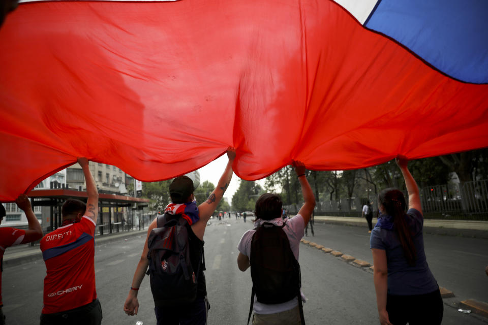 Anti-government demonstrators carry a Chilean flag during a general strike in Santiago, Chile, Wednesday, Oct. 23, 2019. Protesters have taken to the streets as an apology from President Sebastian Pinera and promises of reform failed to quell turmoil that has led to looting, rioting and at least 18 deaths. (AP Photo/Rodrigo Abd)