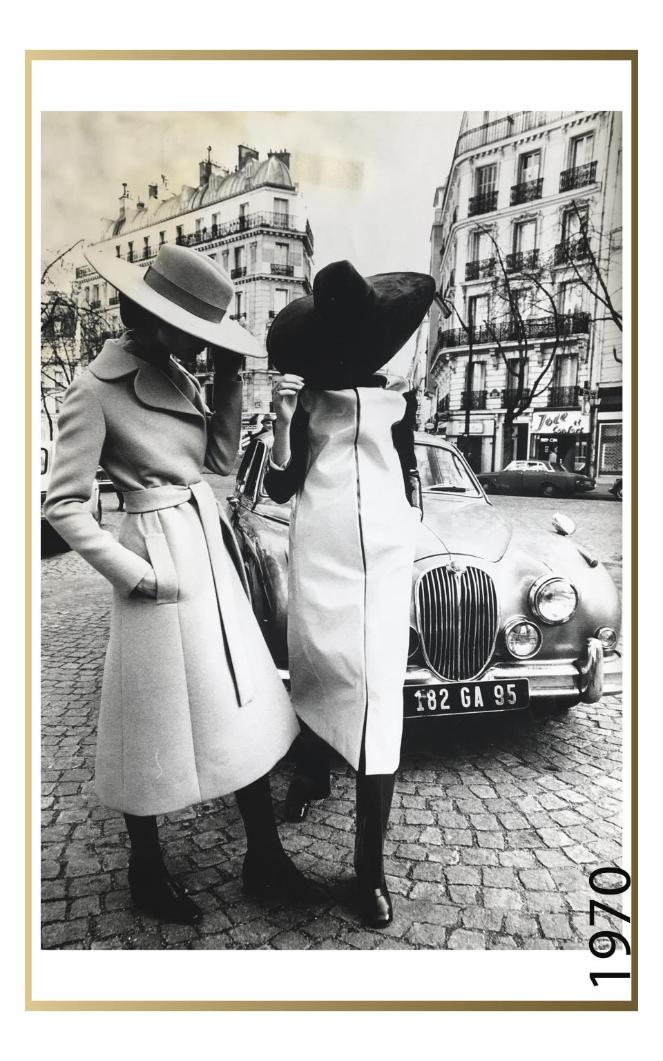 Two models posing on the streets of Paris, in large-brimmed suede and felt hats, paired with a belted, wool, knee-length coat and a vinyl, knee-length, raincoat, over dark-colored pants and shoes, from the Jay Jaxon spring 1970 collection for Maison Jean-Louis Scherrer, 1970. - Credit: Photographer Unknown, Editorial Image, 1970, Maison of Jean-Louis Scherrer, Jay Jaxon’s Portfolio, Bequest of Lloyd Hardy, Rachel Fenderson Collection, 2017