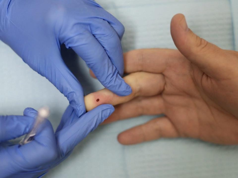 two gloved hands administering a finger prick