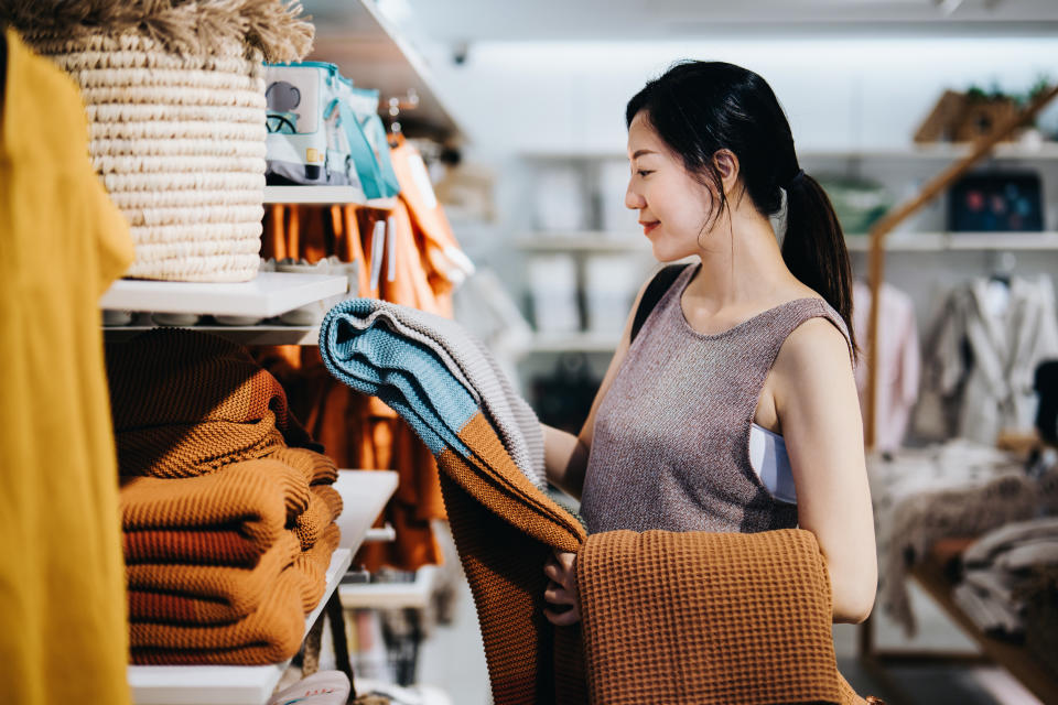 A young woman shopping for home decor in a store holds a blanket she is considering purchasing