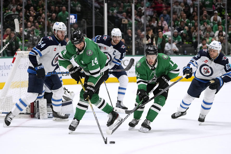 Dallas Stars left wing Jamie Benn (14) and center Logan Stankoven (11) work to take control of the puck in front of Winnipeg Jets' Dylan Samberg (54), Adam Lowry (17) and Nino Niederreiter (62) during the first period of an NHL hockey game in Dallas, Thursday, Feb. 29, 2024. (AP Photo/Tony Gutierrez)