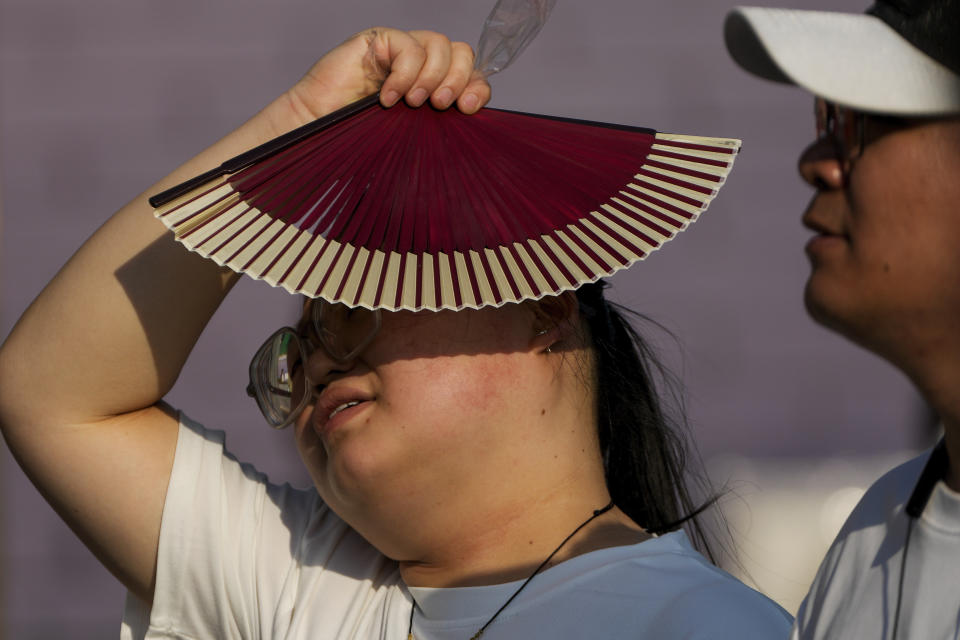 A woman uses a fan to block from the sun as she walks with her companion in an unseasonably hot day in Beijing, Sunday, June 16, 2024. China is being buffeted by two weather extremes, with heavy rain and flooding in parts of the south and a heat wave and potential drought in the north. (AP Photo/Andy Wong)