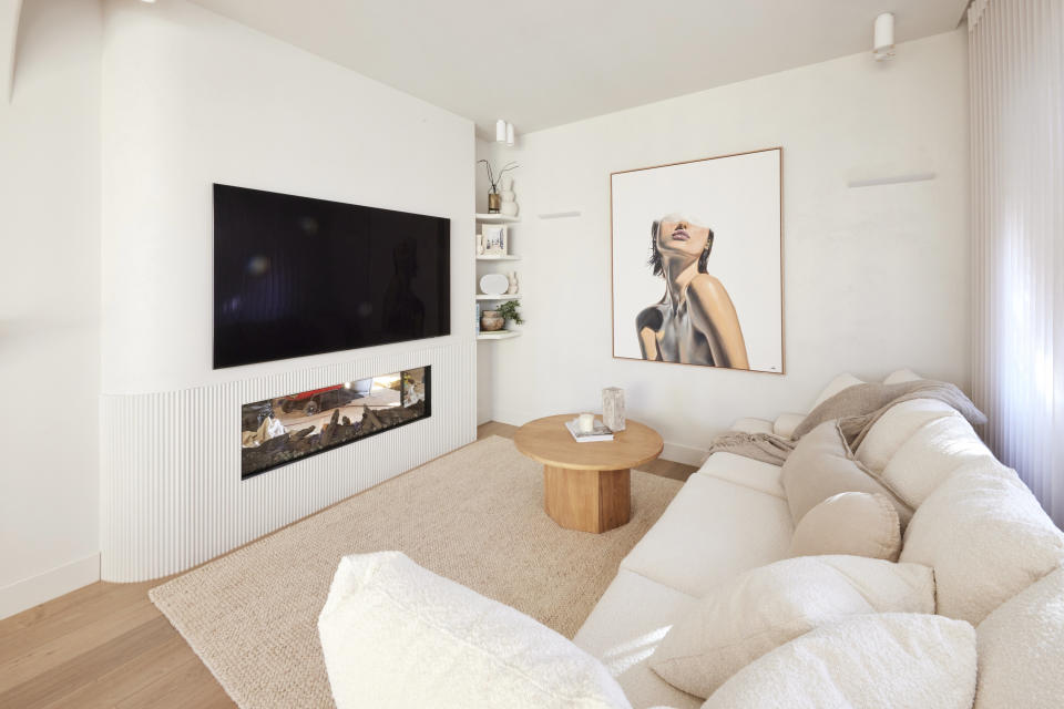 A shot of the living room with a white lounge on the right, a large picture of a woman on the back wall and the tv to the left.