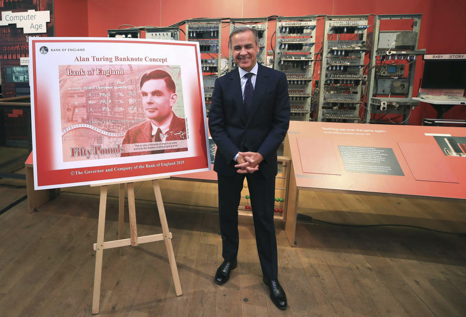 Governor of the Bank of England, Mark Carney poses for a photo with the artwork for the concept of the new 50 pound notes, after announcing that Second World War code-breaker Alan Turing has been selected to feature on the new notes, at the Science and Industry Museum, in Manchester, England, Monday July 15, 2019. The Bank of England has chosen codebreaker and computing pioneer Alan Turing as the face of the country’s new 50 pound note. Governor Mark Carney said Monday that Turing was “a giant on whose shoulders so many now stand.” Turing’s work cracking Nazi Germany’s secret communications helped win World War II, but after the war he was prosecuted for homosexuality, and died in 1954 after eating an apple laced with cyanide. (Peter Byrne/PA via AP)