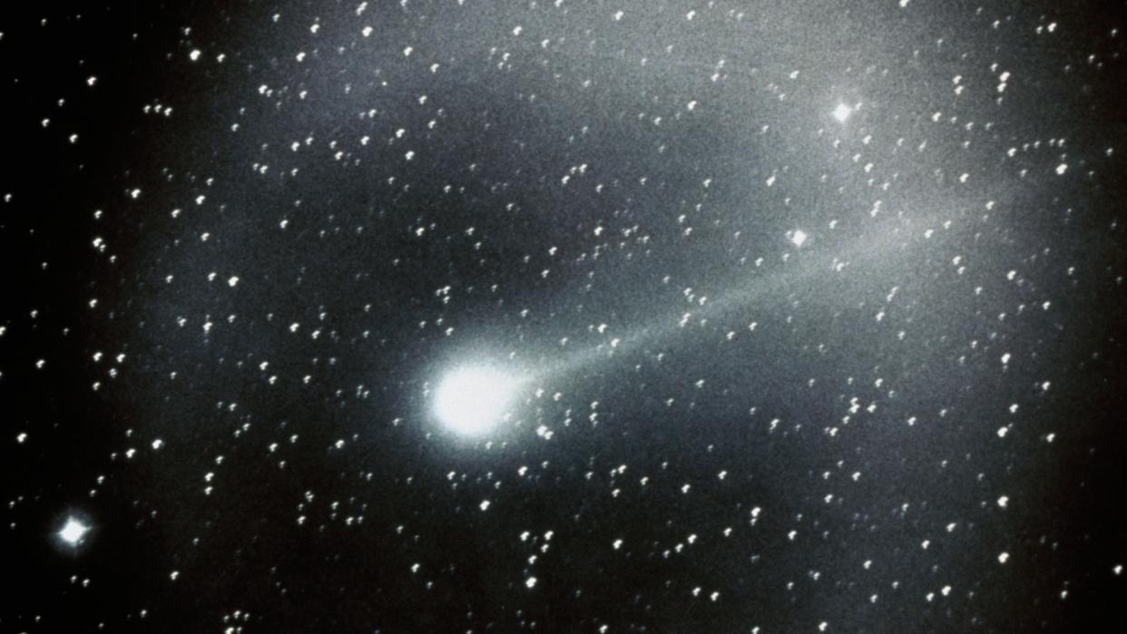  A bright comet streaks through the night sky, leaving a cloudy trail behind it. 