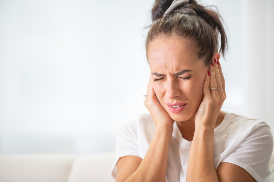 A woman with her eyes closed and her hands over her ears