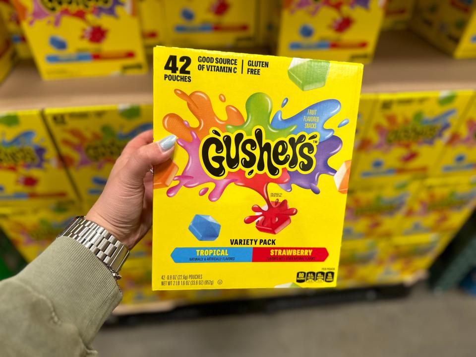 A hand holds a bright-yellow box of Gushers with illustrations of the candy on the front