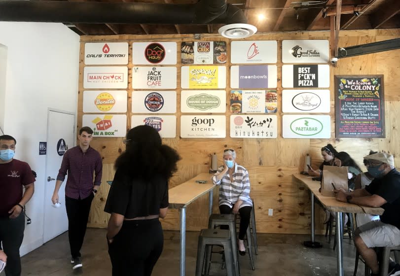 SANTA MONICA, CA - JULY 1, 2021 - - Customers wait for their food at Order Colony in Santa Monica on July 1, 2021. Order Colony, a new use of commercial real estate that allows dozens of restaurant brands to operate out of a single kitchen space. The acceleration of delivery and takeout as well as the economic stress caused by the pandemic have led more restaurants to participate. (Genaro Molina / Los Angeles Times) FYI EDITOR: WE DIDN'T HAVE PERMISSION TO PHOTOGRAPH INSIDE THE BUSINESS. I MADE THIS IMAGE WITH MY iPHONE THROUGH A SIDE DOOR THAT LEADS TO THEIR OUTDOOR PATIO AT THE BUSINESS. I WAS STANDING ON THEIR PROPERTY WHEN I MADE THIS IMAGE.