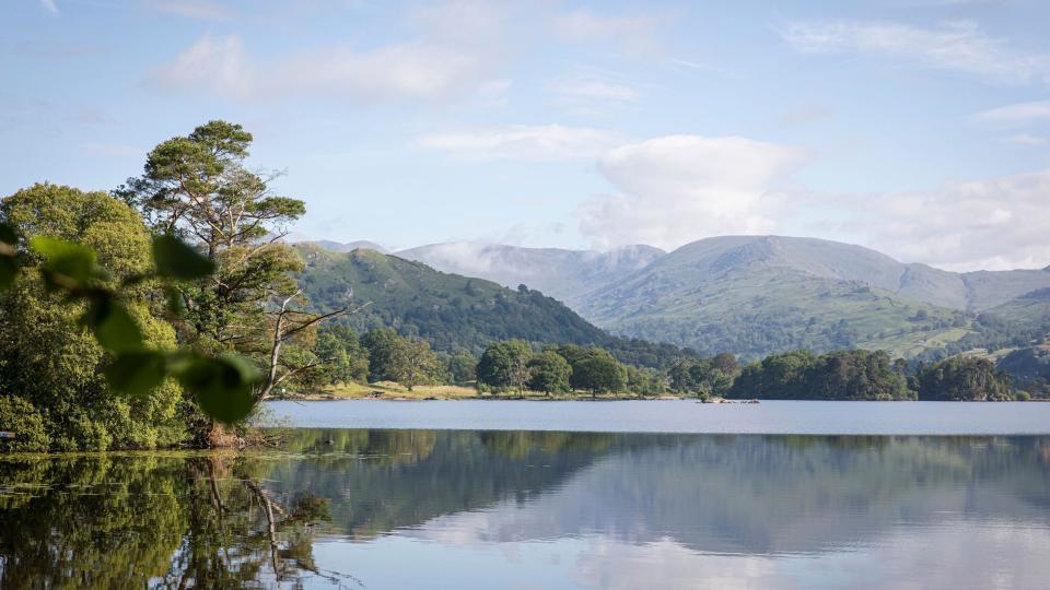 A panoramic view of a still lake, with hills and trees reflected in its vast waters.