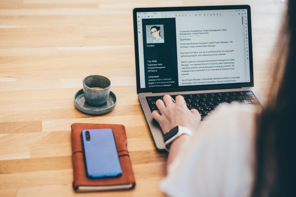 Person at work viewing a LinkedIn profile on laptop, near coffee cup, phone, and notebook