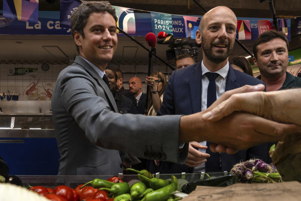French Prime Minister Gabriel Attal, center campaign with local candidate for the second round of the legislative election Stanislas Guerini, right, Tuesday, July 2, 2024 at a market in Paris. After France's far-right National Rally surged into the lead in the first round of legislative elections, some European neighbors on Monday cast a wary eye on the latest country to veer to the right on the continent. (AP Photo/Louise Delmotte)