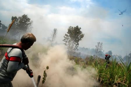 Local residents try to extinguish a fire as a helicopter from the Indonesian National Disaster Management (BNPB) is seen overhead in Pekanbaru, Riau province, Sumatra island, Indonesia August 10, 2016 in this photo taken by Antara Foto. Picture taken August 10, 2016. Antara Foto/Rony Muharrman/ via REUTERS