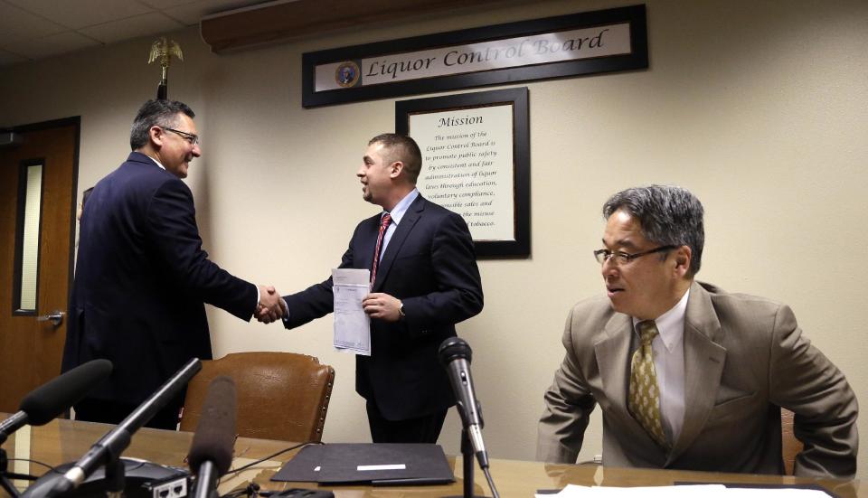 Sean Green, center, is congratulated by Washington State Liquor Control Board Director Rick Garza, left, as board member Chris Marr returns to his seat after Green received his new legal marijuana license Wednesday, March 5, 2014, in Olympia, Wash. Green, a medical marijuana dispensary operator from Spokane, was issued the producer-processor license under the state's recreational pot law at the Liquor Control Board meeting. (AP Photo/Elaine Thompson)