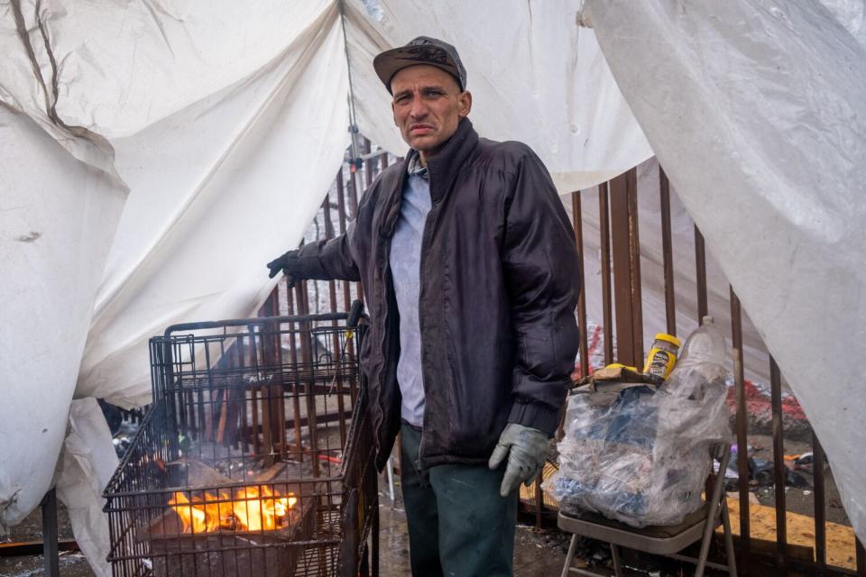 Carlos Parra Aguiar stands next to a grocery cart fire he built to stay warm.