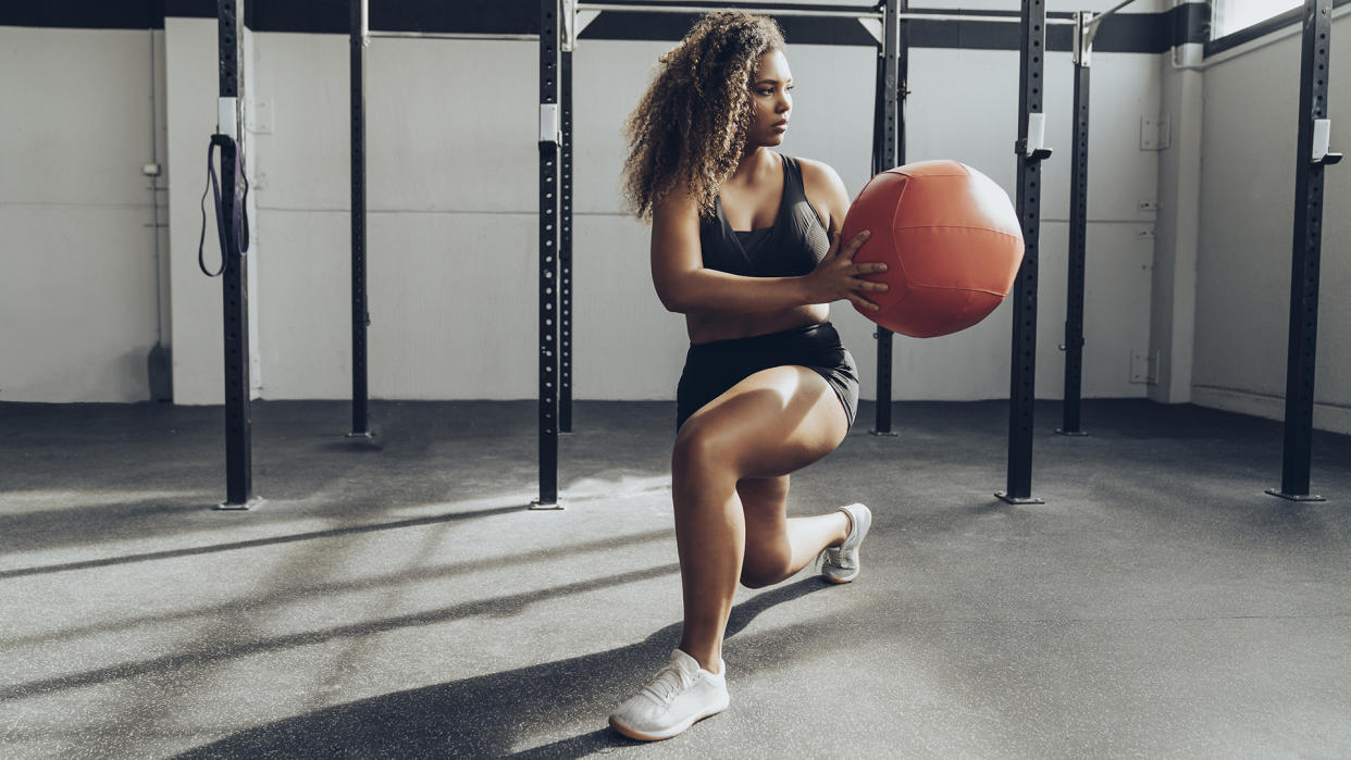  Young woman exercising with medicine ball in gym. 