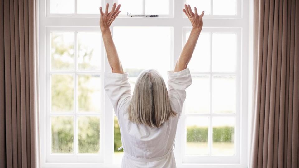 Una mujer estirándose frente a una ventana.