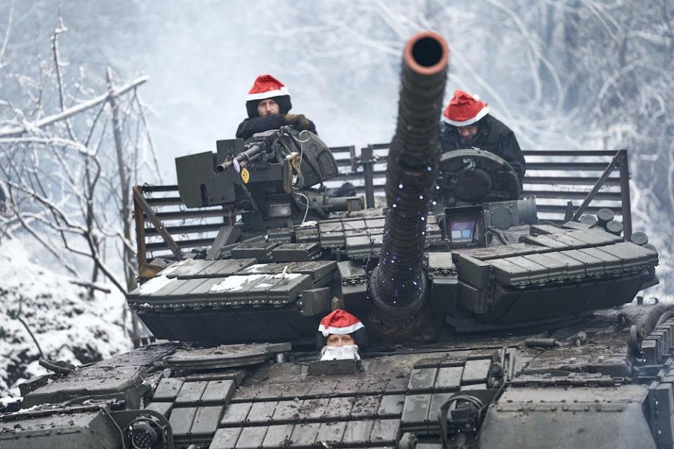 Three soldiers dressed in Santa hats crew a T-64 battle tank, wrapped in Christmas lights, against a snowy background on December 24, 2023.