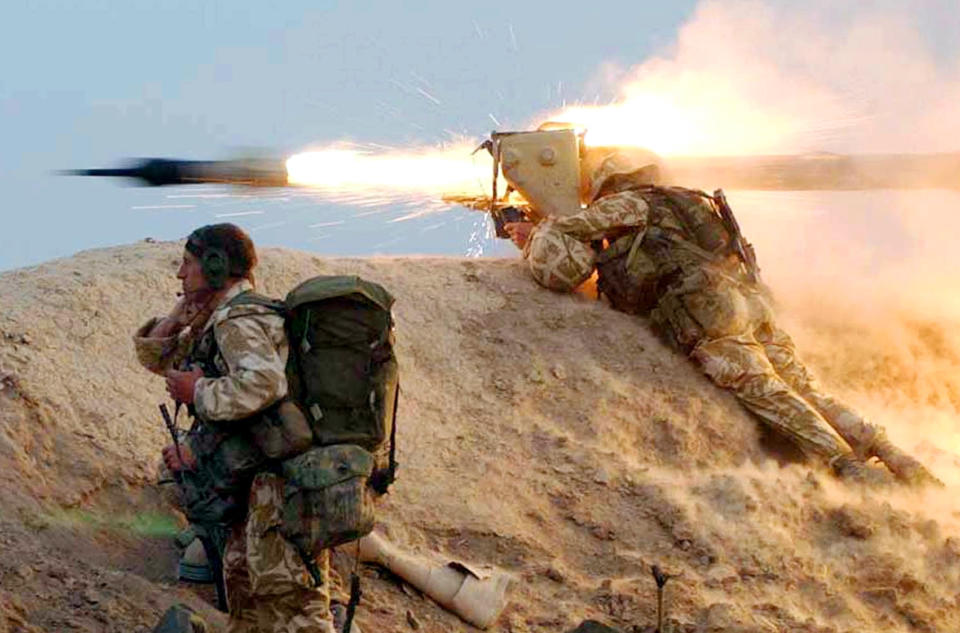 Two British Royal Marines crouch on an embankment in the desert as a rocket whizzes by.