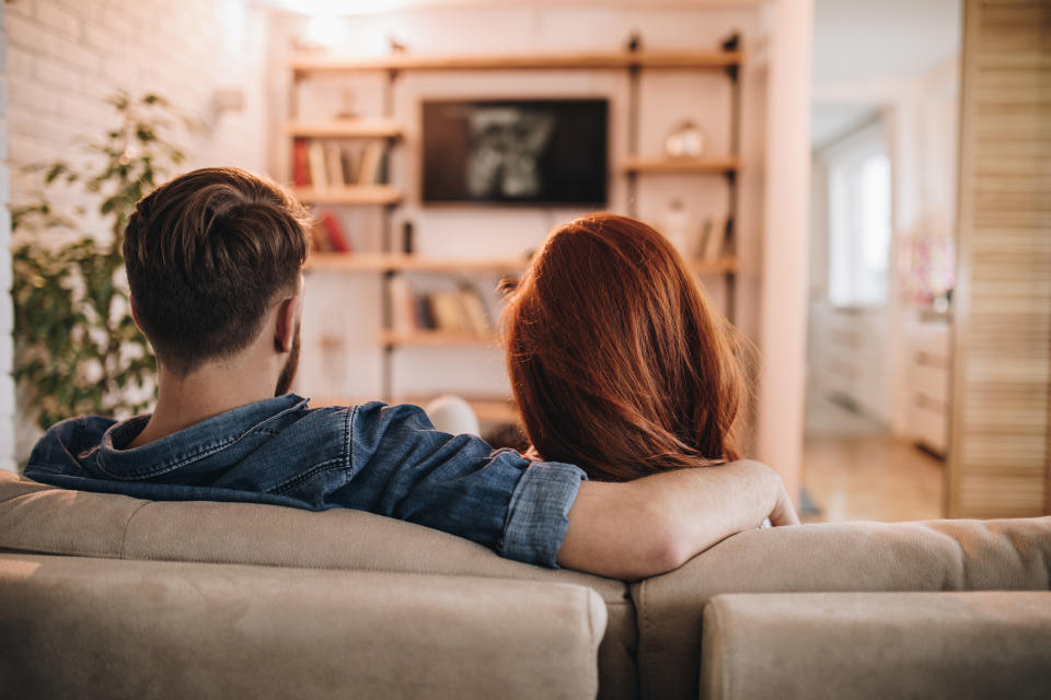 Two people sitting close on a sofa, watching TV, viewed from behind