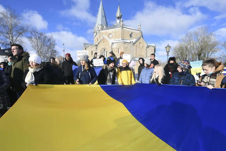 Unas personas sostienen una enorme bandera nacional ucraniana durante una protesta en apoyo a Ucrania frente al Consulado General de Rusia en Narva, Estonia, el sábado 26 de febrero de 2022.