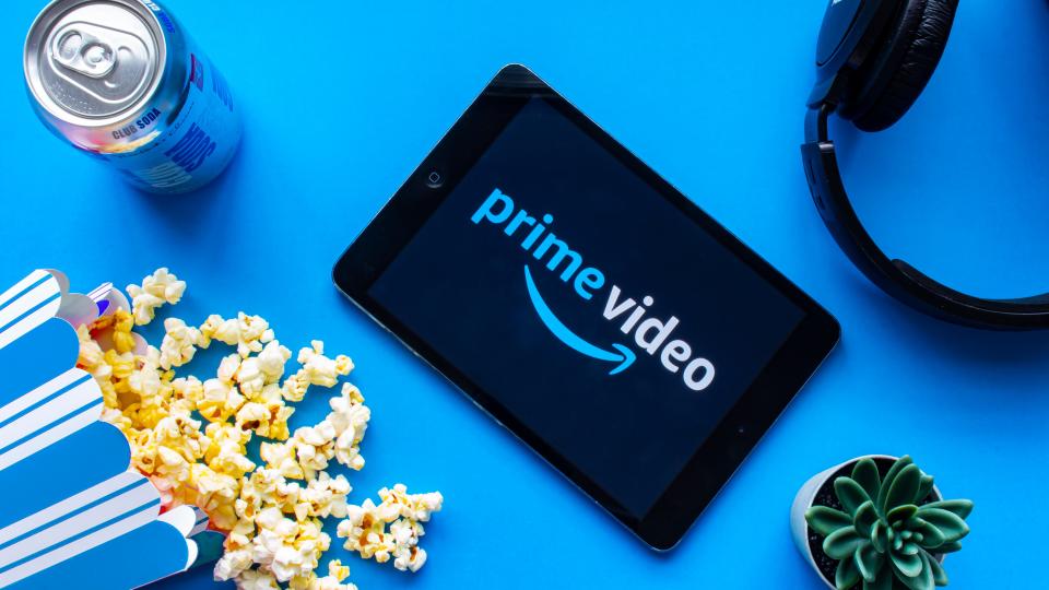  Prime Video logo appears on a tablet surrounded by a can of soda, spilled popcorn, headphones and a cactus. 