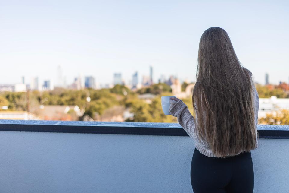 Woman drinking coffee and looking off into the Austin, Texas skyline.