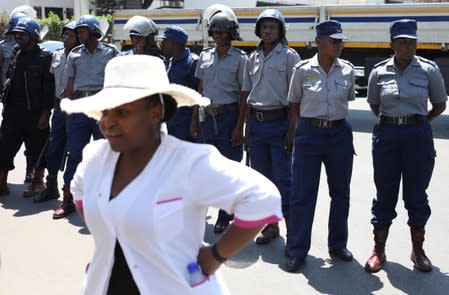 A nursing sister looks on as Police officers stand guard during a protest by doctors over the disappearance of the leader of their union in Harare