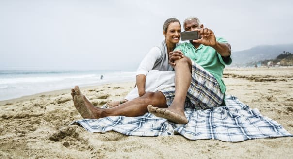 Senior African American couple having fun with smartphone on beach