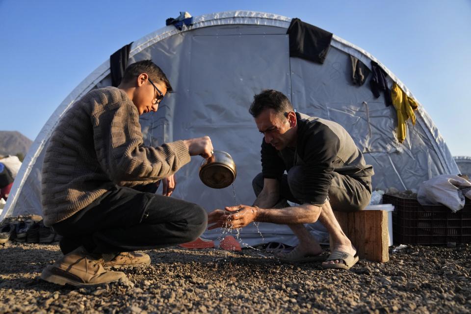 FILE - A boy, left, helps his father washing his hands at a makeshift camp where they settle after they lost their house in a devastated earthquake, in Iskenderun city, southern Turkey, on Feb. 14, 2023. Hundreds of thousands of people are seeking shelter after the Feb. 6 earthquake in southern Turkey left homes unlivable. Many survivors have been unable to find tents or containers dispatched to the region by the government and aid agencies, Instead they have sought refuge in any structure that can protect them from the winter conditions, including greenhouses, rail carriages and factories. (AP Photo/Hussein Malla)