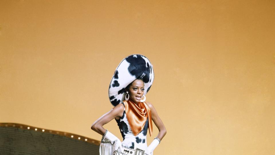 diana ross dressed in a cowprint cowgirl outfit with an orange scarf around her neck